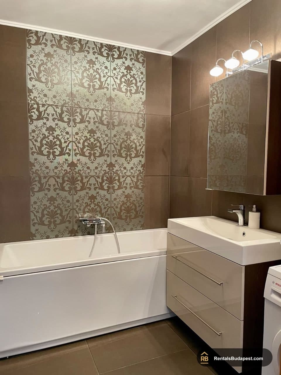 Brown-tiled bathroom with patterned wall tiles, white bathtub, floating vanity and wall-mounted lights, Sobieski János utca