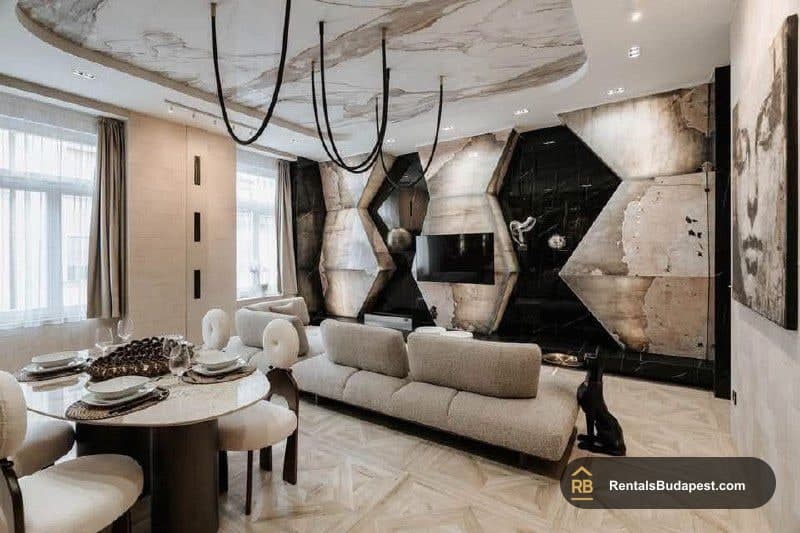 Living room with a round marble dining table, beige sofa, black and marble geometric feature wall, and hanging black pendant lights