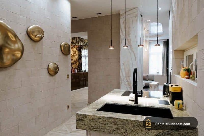 Kitchen counter with black sink and granite worktop, gold wall discs, pendant lights, and a view into the living room