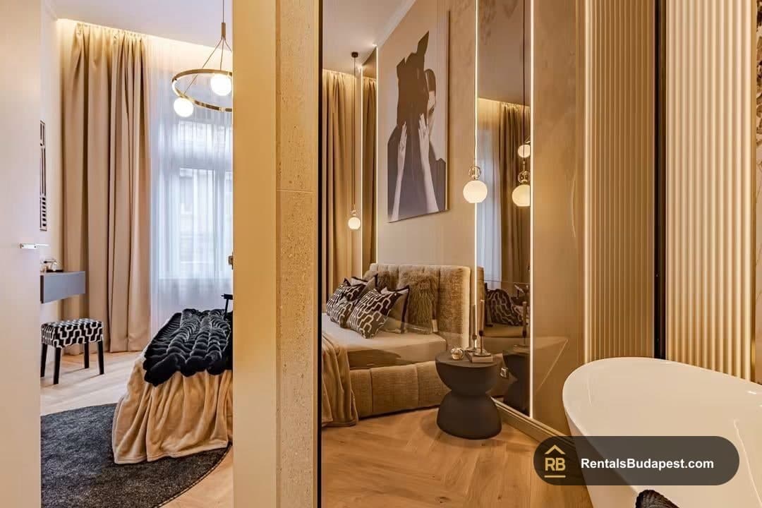 View from hallway into bedroom with bed, pendant lamps, floor-length beige curtains, and glimpse of freestanding tub, Falk Miksa utca
