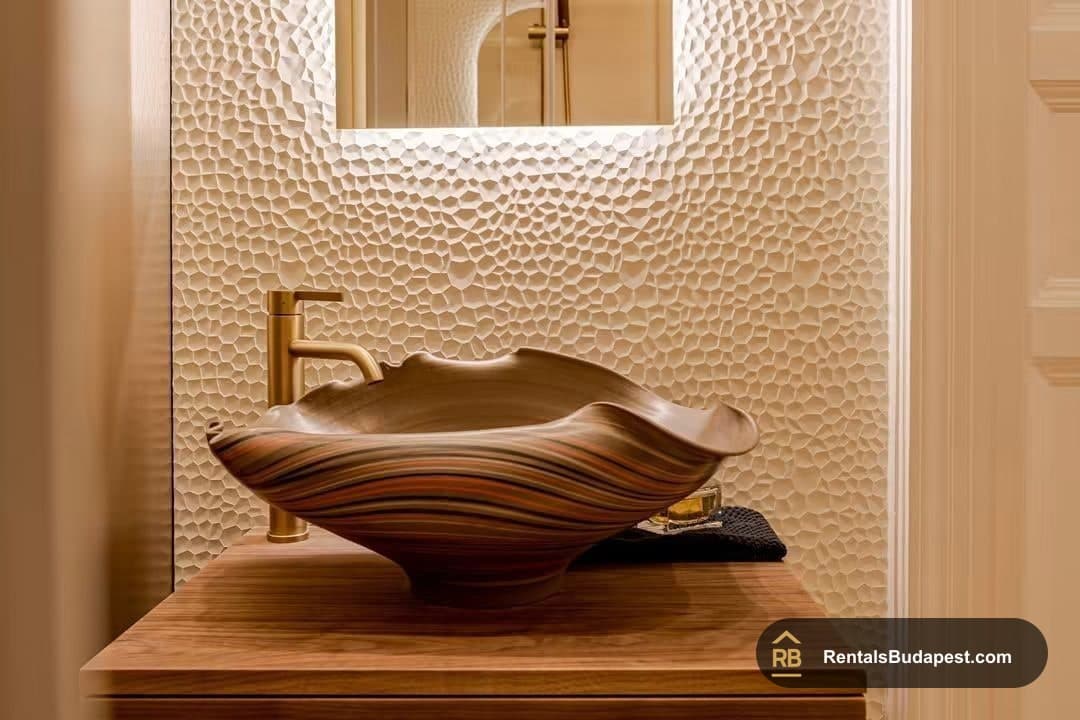 Carved wooden basin on walnut vanity beside textured wall and brass tap, Falk Miksa utca