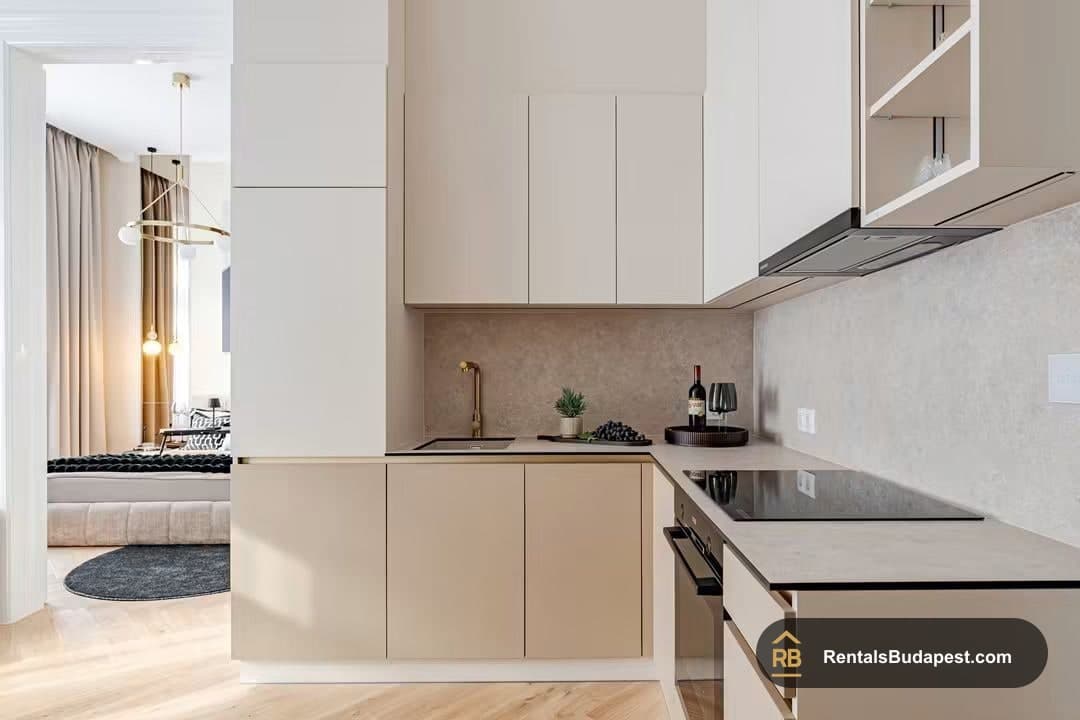 Cream kitchen cabinets, induction hob and wine bottle beside open doorway to bedroom, Falk Miksa utca