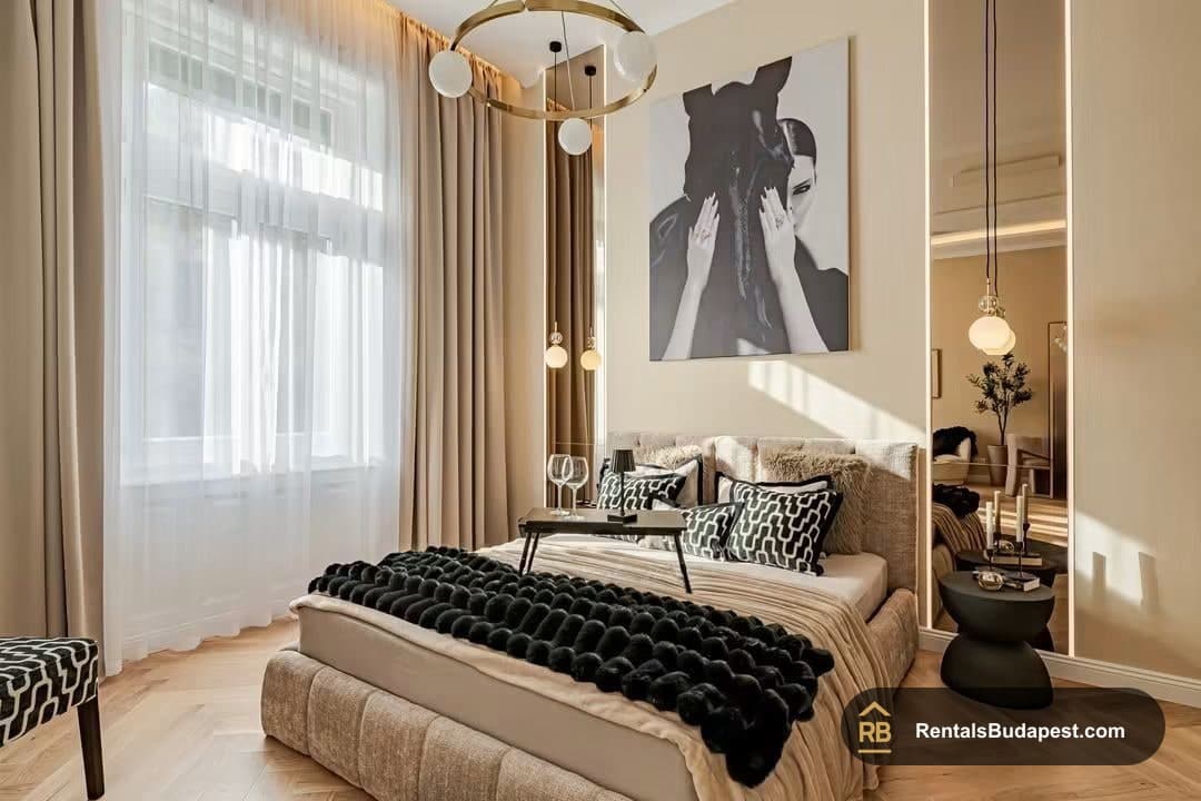 Bedroom with sheer curtained window, round brass chandelier and black fur throw on bed, Falk Miksa utca