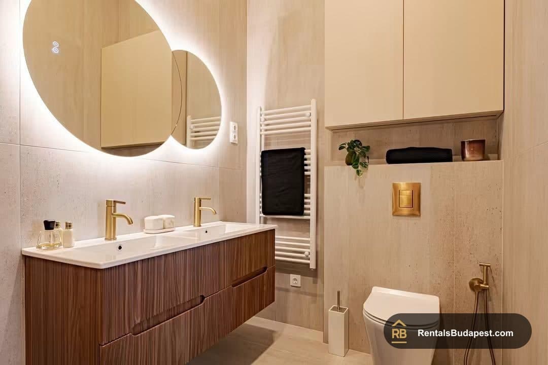 Modern bathroom with a double vanity, backlit round mirrors, gold fixtures, and a heated towel rail, on Falk Miksa utca