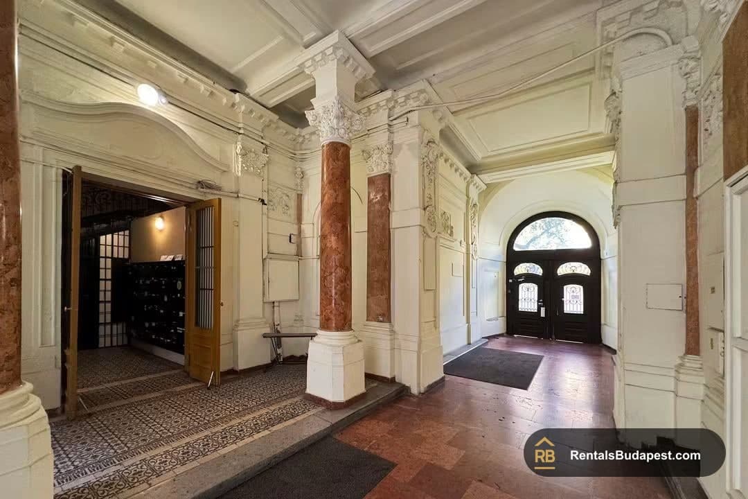 Ornate building entrance hall with marble columns, arched wooden doors, and a patterned tile floor, on Falk Miksa utca