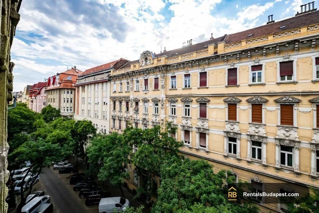 Street view of tree-lined Falk Miksa utca with parked cars and ornate cream-colored historic apartment facades