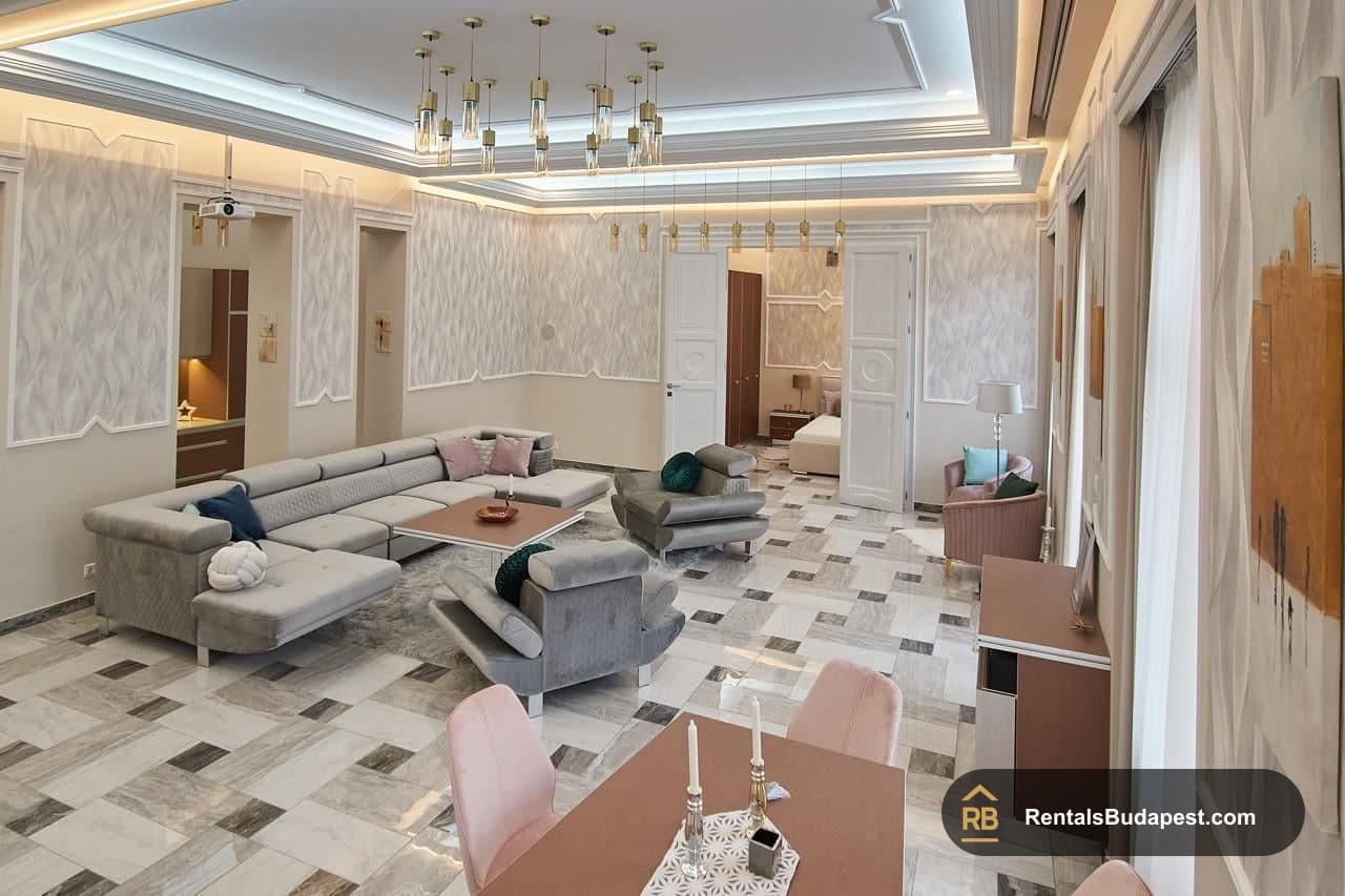 Open living room with grey sectional sofa, pink accent chairs, marble-patterned floor and pendant lights, Szent István körút