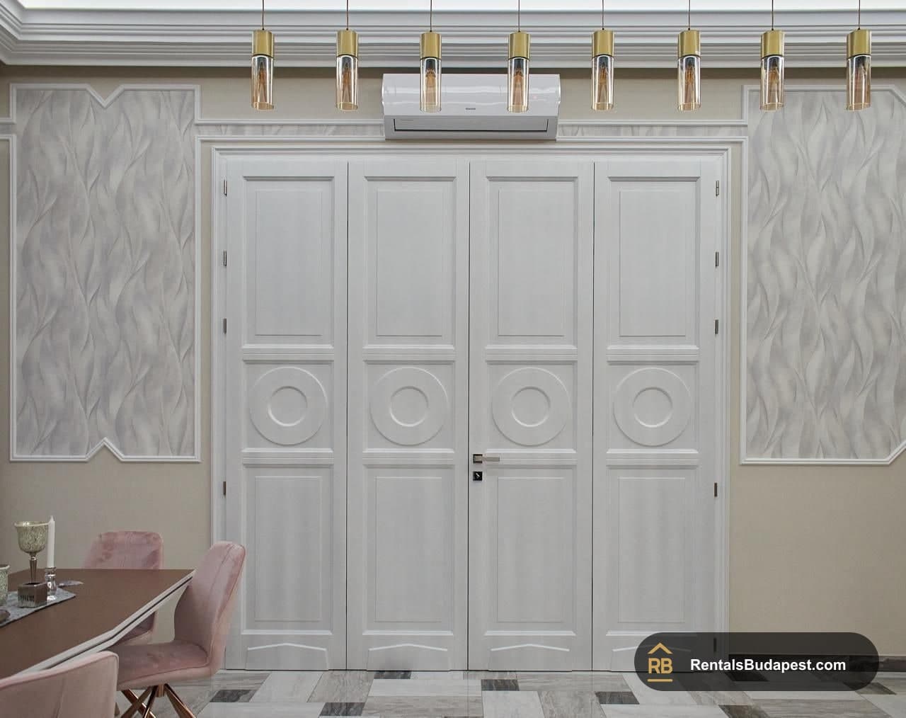 White paneled double doors framed by decorative wall panels, pendant lights above and pink dining chairs at left, Szent István körút