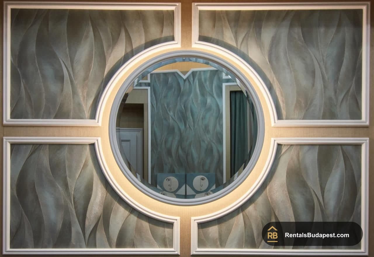 Circular mirror set within a white-framed wall panel with wave-textured grey wallpaper, Szent István körút