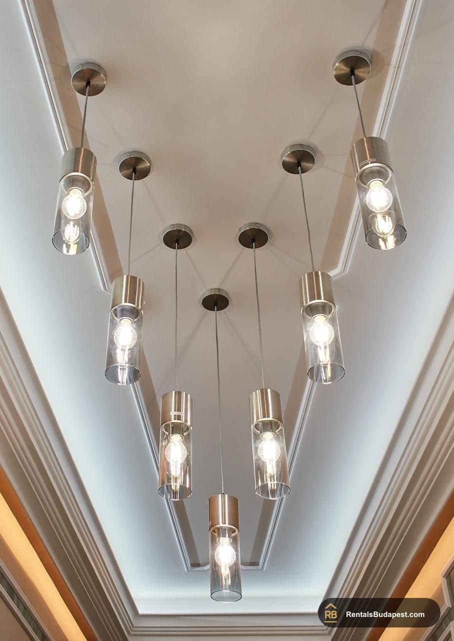 Ceiling view of a cluster of clear glass pendant lights hanging in a V-shaped arrangement, Szent István körút