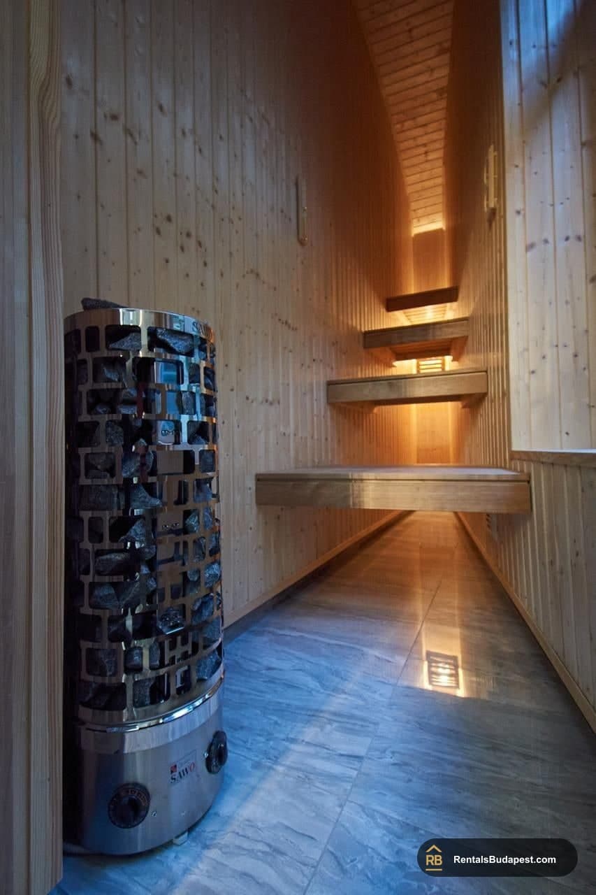 Sauna with wood-paneled walls, tiered wooden benches and a stone heater beside them