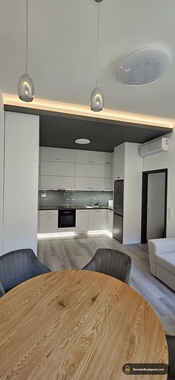Open-plan kitchen with white cabinets, pendant lights, and round wooden dining table in front
