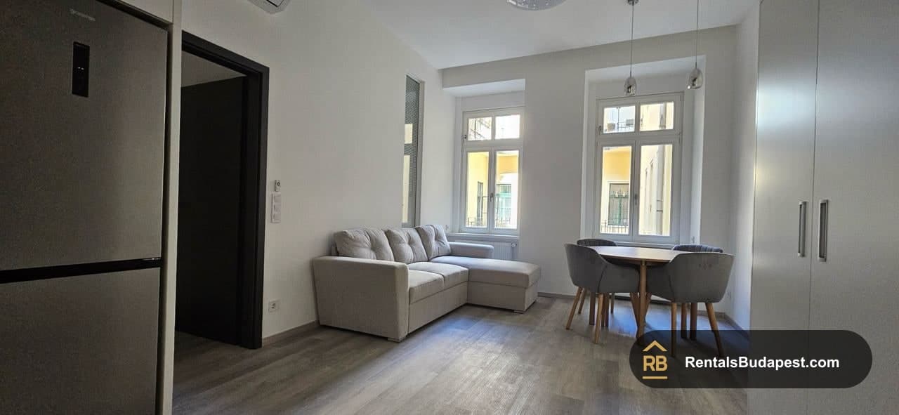 Living room with grey corner sofa, dining table with grey chairs, and bright windows