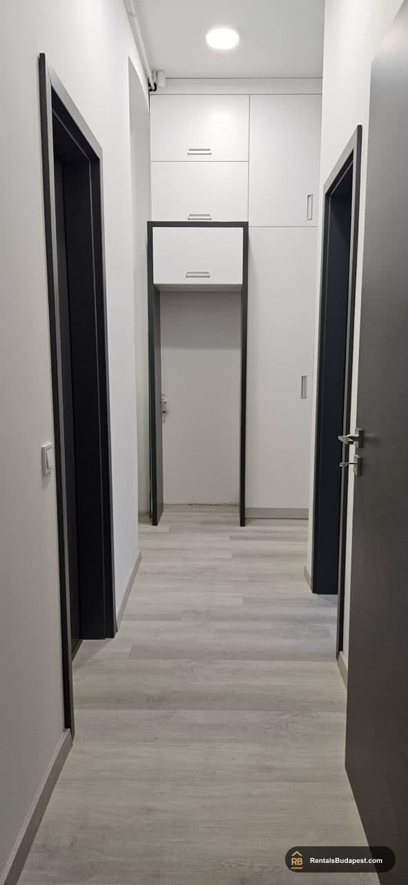 Narrow hallway with dark-framed doors, grey laminate floor, and white storage cabinets overhead