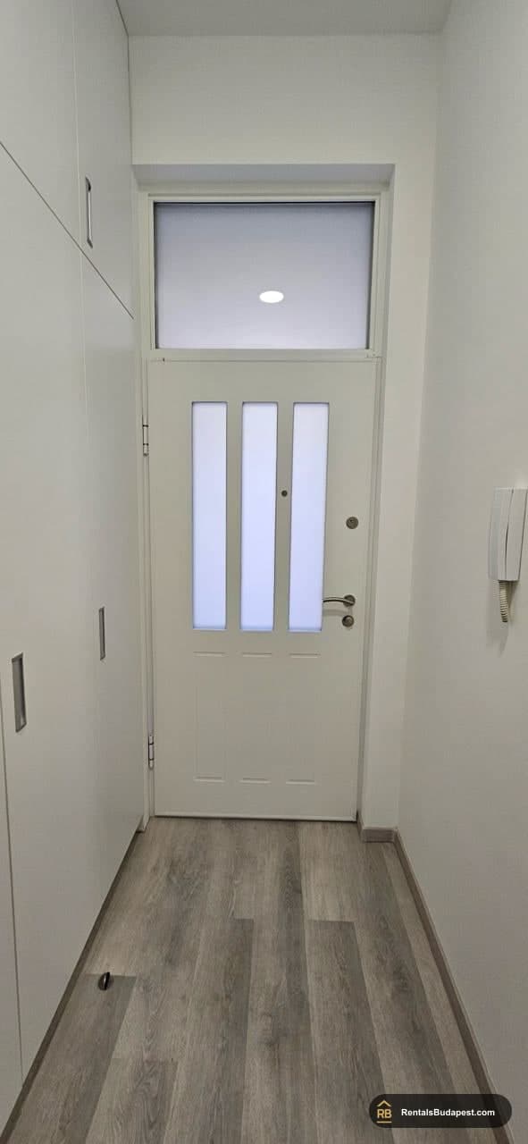 Apartment entrance with frosted glass door, white wardrobe panels, and intercom panel on wall