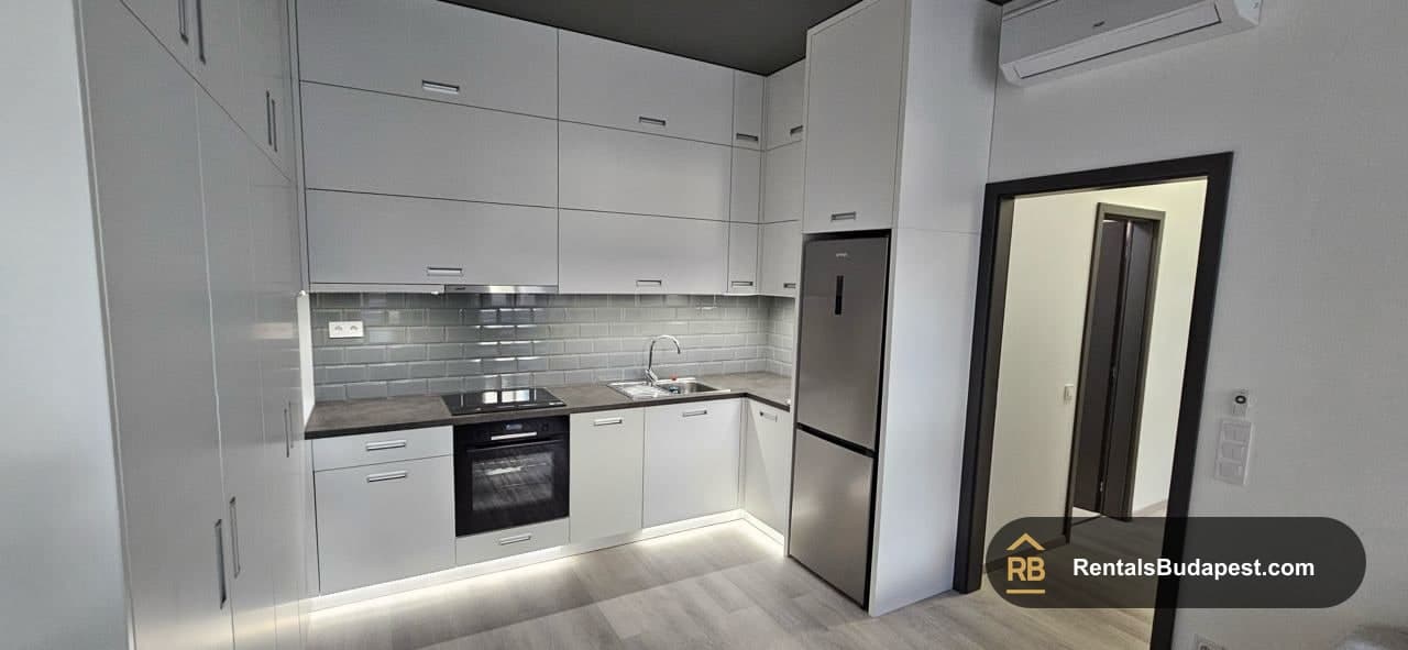 White kitchen with grey tiled backsplash, induction hob, black oven and stainless steel fridge, Museum street