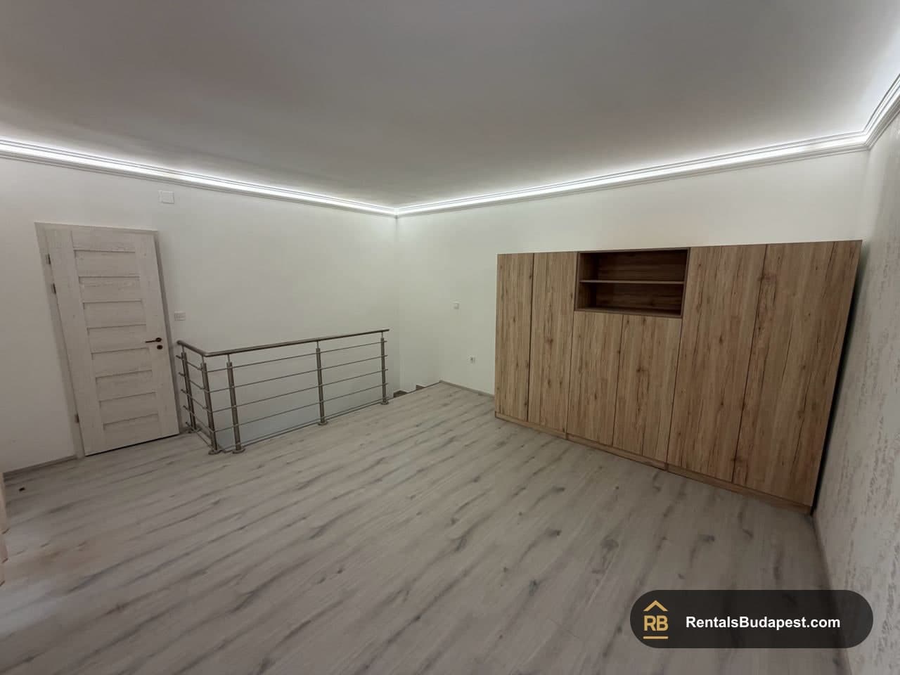 Empty upper room with large wood-effect built-in wardrobe, steel stair railing and light wood flooring, Szent István körút