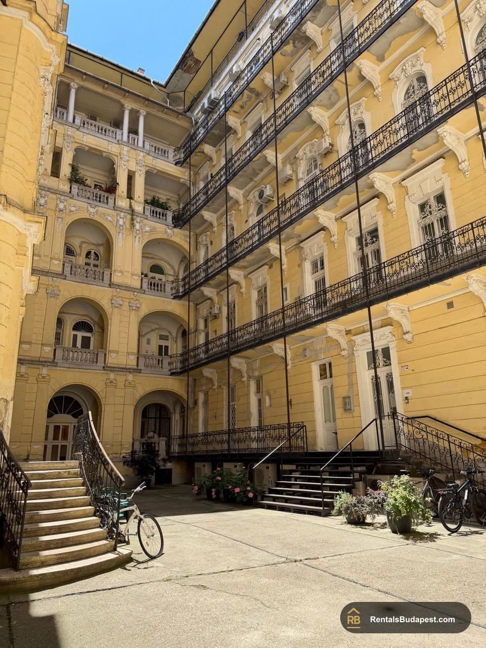 Courtyard of a yellow historic apartment building with multi-level iron balconies, arched windows and bicycles, Szent István körút