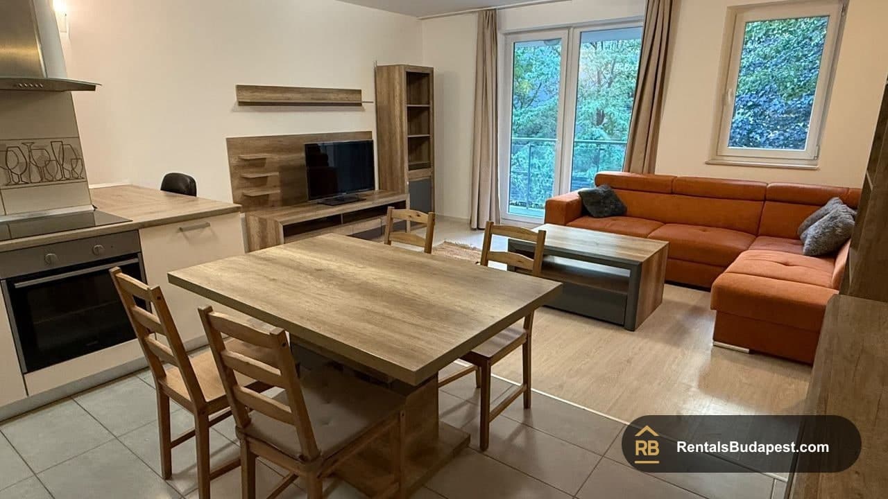 Open-plan dining area with wooden table, chairs, kitchen oven and orange sofa, Viola utca