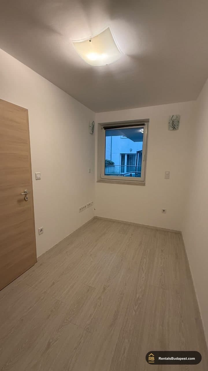 Empty bedroom with wood-effect flooring, ceiling light and window facing neighbouring building, Viola utca
