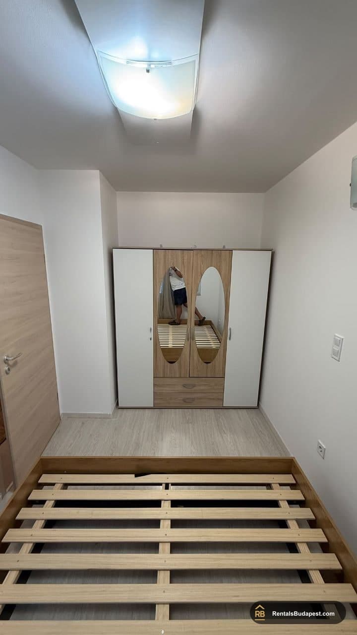 Bedroom with white and wood wardrobe and bare bed frame against wall, Viola utca