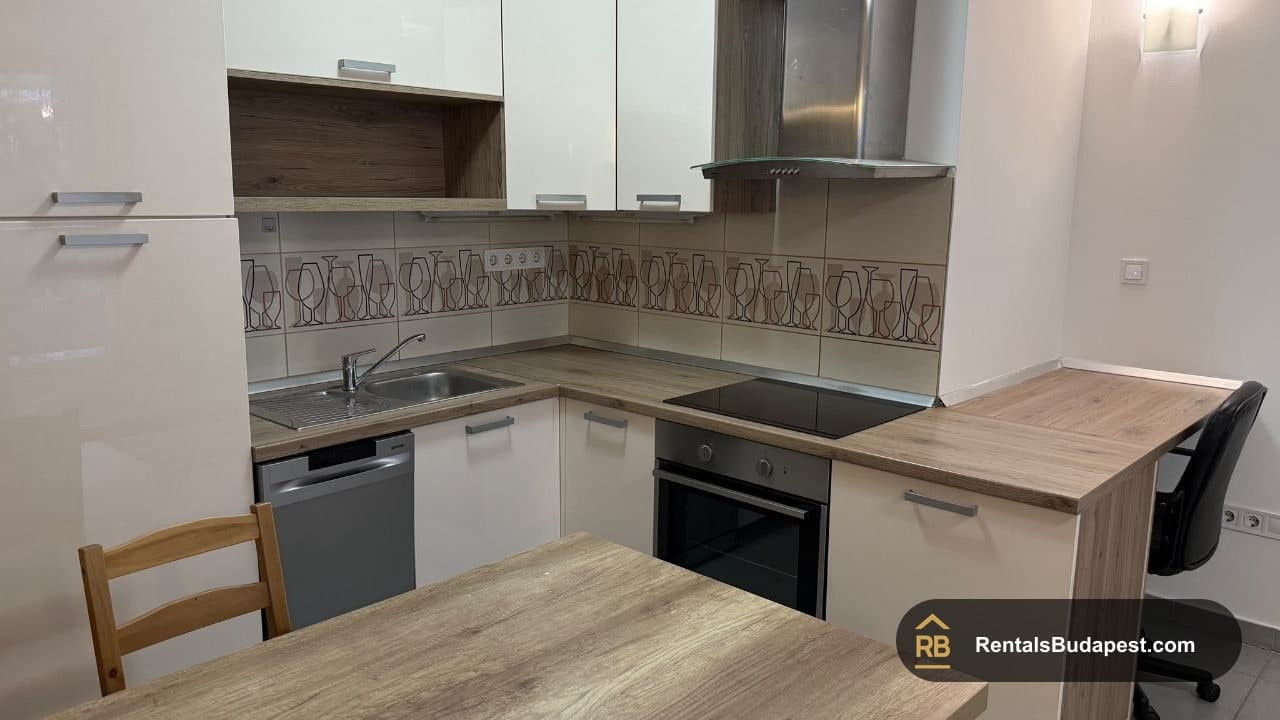 Kitchen with white cabinets, wood-effect countertops, built-in oven and hob, and a dining table, Viola utca