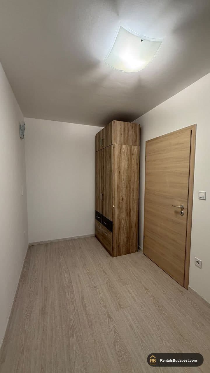 Empty bedroom with light laminate flooring, a tall wooden wardrobe, and a wooden door, Viola utca