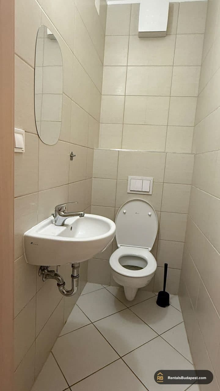 Narrow guest toilet with wall-hung toilet, corner sink, and beige tiled walls, Viola utca