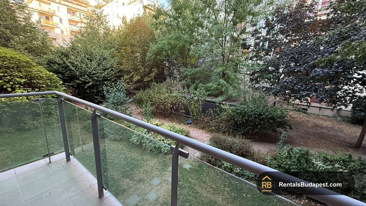 View from a glass-railed balcony over a leafy courtyard garden with trees and shrubs, Viola utca