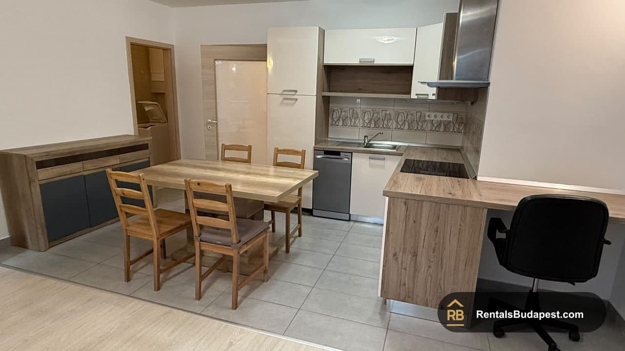 Living room with wooden dining table and chairs, sideboard, open kitchen with white cabinets, and office chair, Viola utca