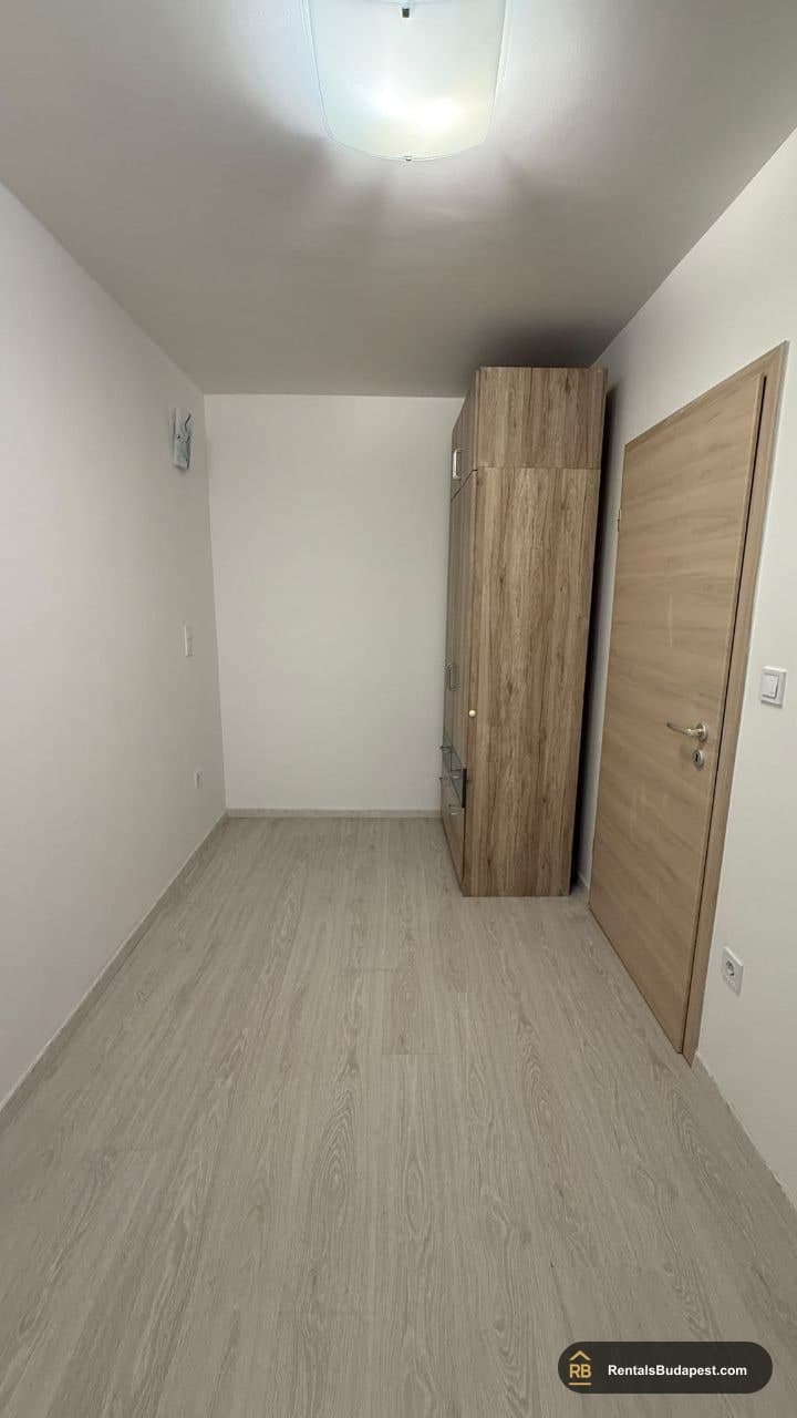 Empty bedroom with light laminate floor, tall wood-effect wardrobe and white walls, Viola utca