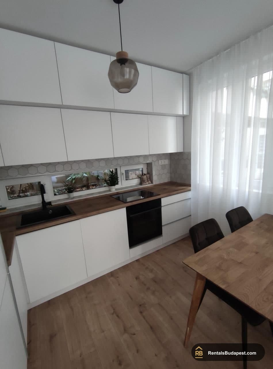 White kitchen with wood-effect countertop, black sink and oven, pendant lamp and wooden dining table, Corvin sétány