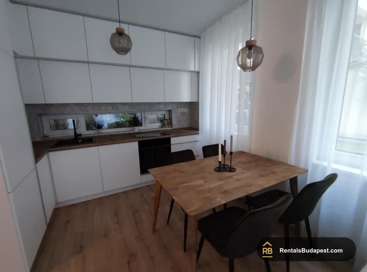 Compact kitchen with white cabinets, black oven and wooden dining table with dark chairs, Corvin sétány