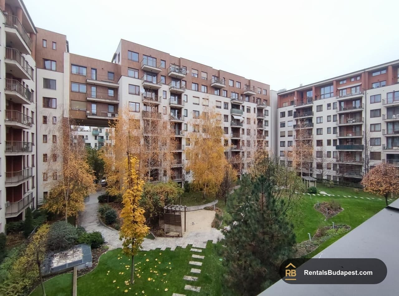 View over a courtyard of residential apartment blocks with autumn trees, lawns and paved paths, Corvin sétány