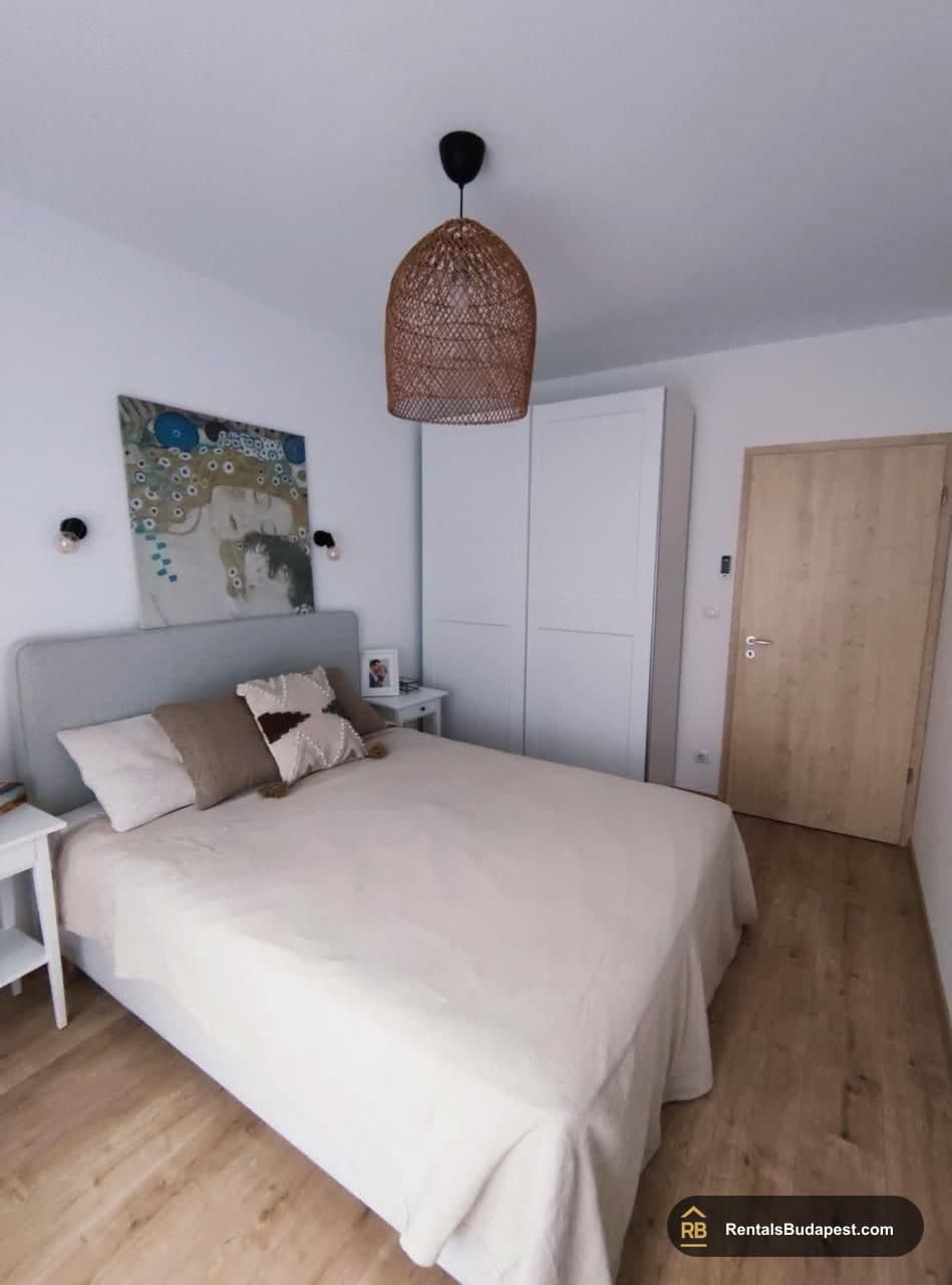 Double bedroom with white bedding, a grey upholstered headboard, a woven pendant lamp, a large abstract painting, and a white wardrobe, Corvin sétány