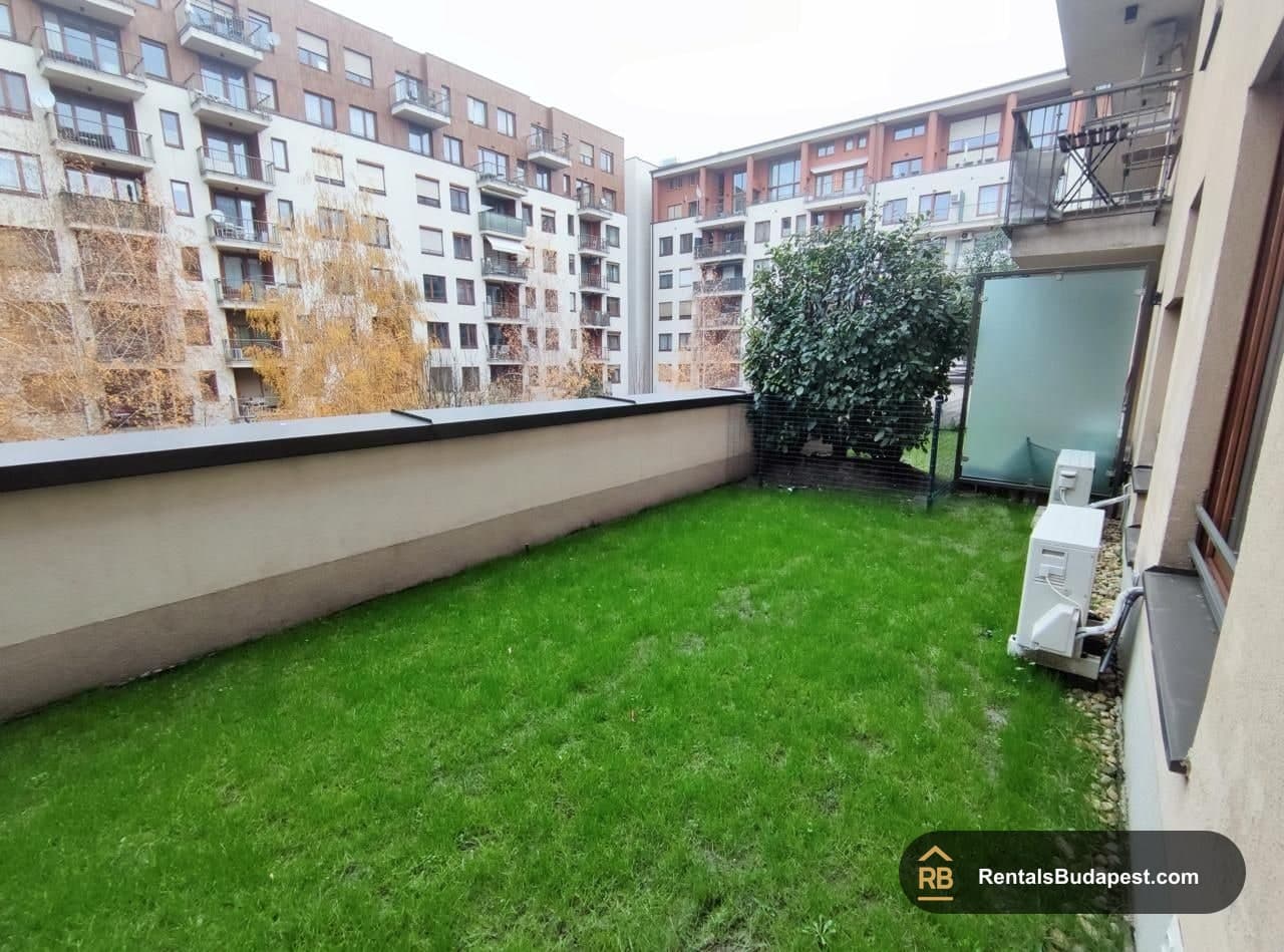 Enclosed grass terrace with a low wall, outdoor air conditioning units, and surrounding apartment blocks, Corvin sétány